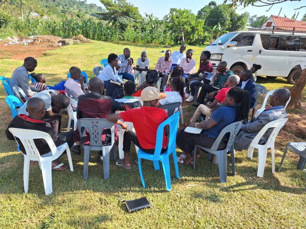 A gathering seated outdoors under the trees